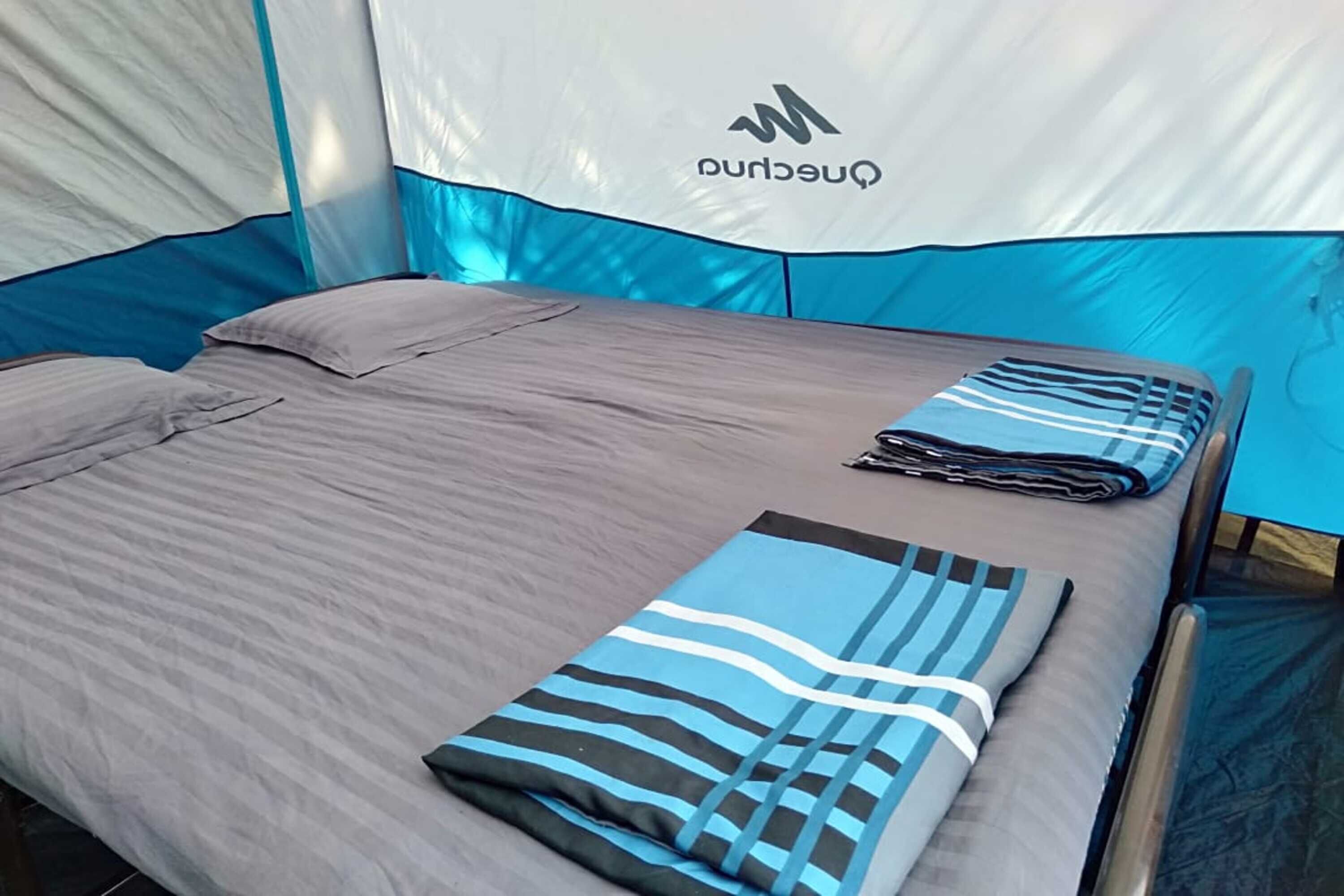 A tented accommodation with a bed, pillows, and a folded blanket.