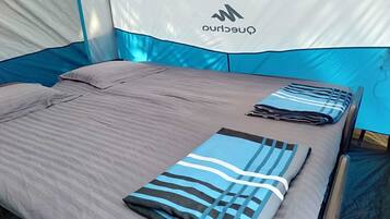 A tented accommodation with a bed, pillows, and a folded blanket.