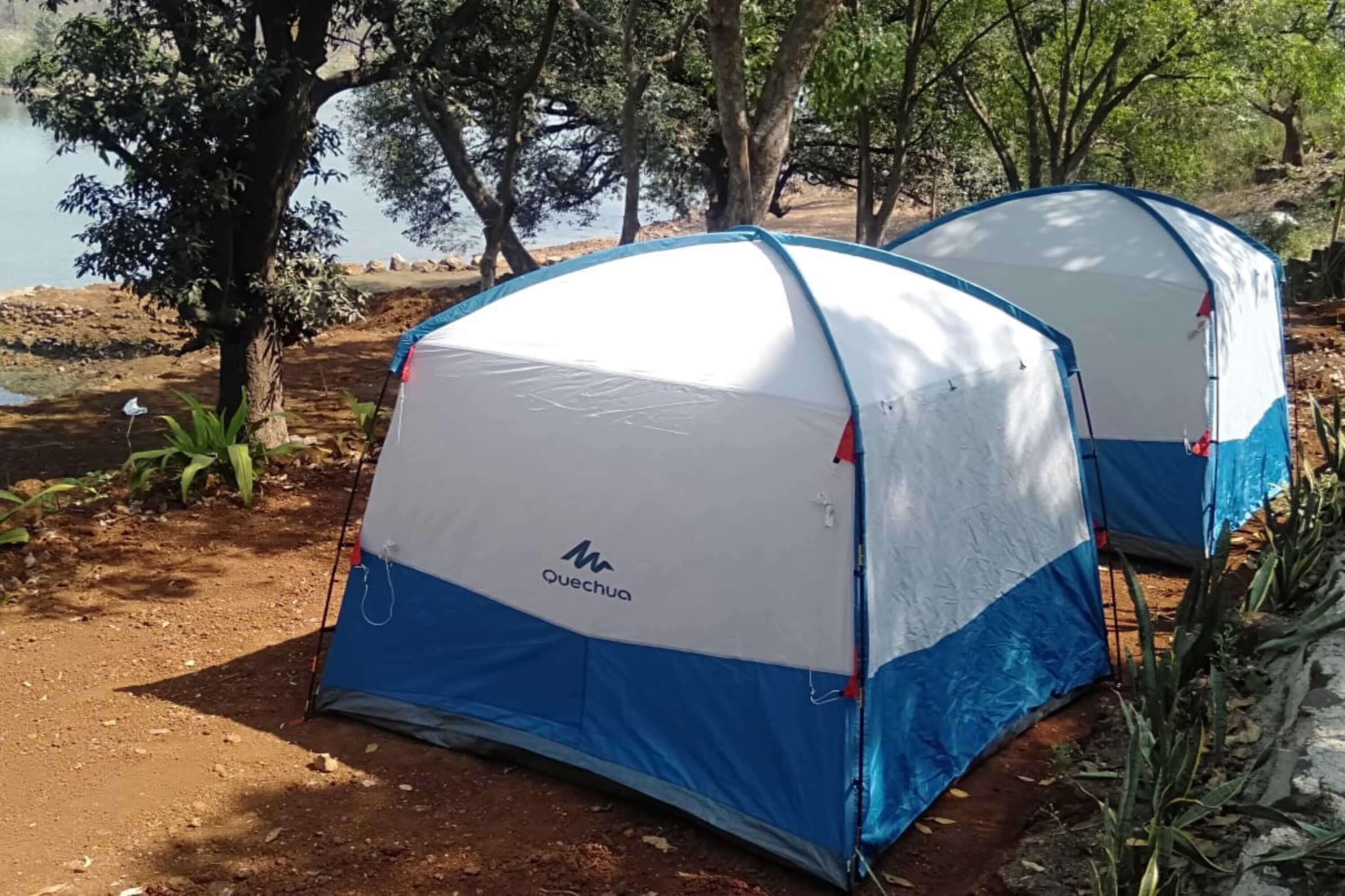 Two Quechua tents set up near a lake, surrounded by trees and vegetation.