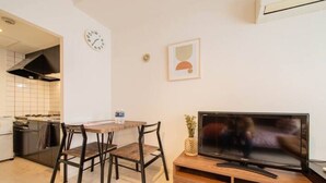 A compact living space with a dining area, a TV on a wooden stand, and a kitchen in the background. - Purple (Sapporo)