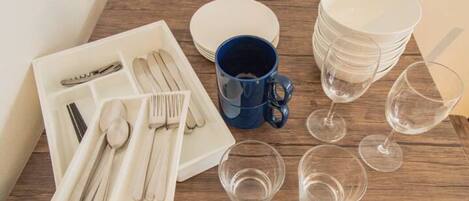 A dining setup with a white plate set, a blue mug, and stacked white plates on a wooden table.