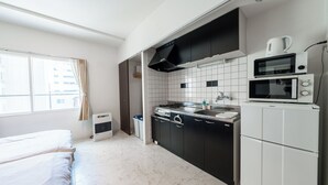 A compact kitchen with a stove, microwave, and sink, adjacent to a bed in a small room with a window. - Yellow (Sapporo)