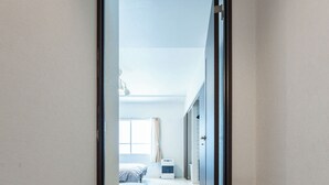 A hallway with a marble floor leading to a bedroom with a bed and a window. - Yellow (Sapporo)