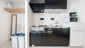 A compact kitchen with black cabinets, a white refrigerator, a microwave, and a stove. There are two trash bins and a wooden shelf above the stove. - Yellow (Sapporo)
