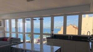 Eine moderne Küche mit großen Fenstern, einem Essbereich mit Glastisch und Meerblick.