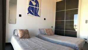 Ein modernes Hotelzimmer mit zwei Einzelbetten, einem großen Fenster und einem modernen, abstrakten Gemälde an der Wand.