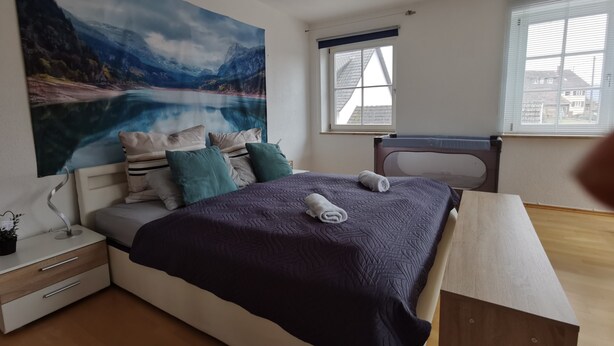 A bedroom with a bed, a nightstand, a bedside table, a window, and a painting on the wall. - Apartment Close to Lake Ferienwohnung Seenah (Sipplingen)