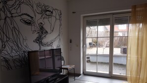 A living room with a large TV, a sofa, and a window with a view of the outside. - Apartment Close to Lake Ferienwohnung Seenah (Sipplingen)