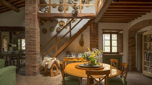Ein Essbereich mit einem runden Holztisch, grünen Polsterstühlen, einer Blumenvase und einer Treppe mit Holzwandleisten und Hüten an der Wand.