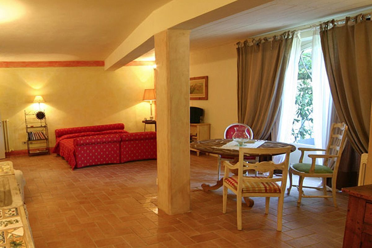 A cozy living room with a red sofa, a wooden dining table with chairs, and a large window with curtains.