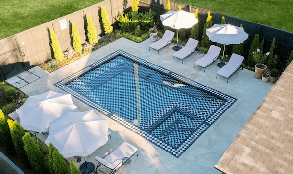 Piscina rectangular con baldosas de diseño ajedrezado, rodeada de sillas de descanso y sombrillas.