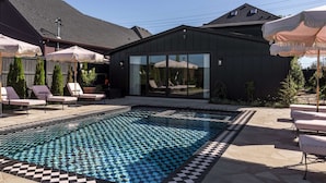 Ein moderner Poolbereich im Freien mit Liegestühlen, einer überdachten Sitzgruppe und einem Gebäude mit großen Fenstern.