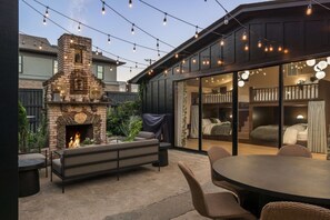 Un patio con chimenea de piedra, mobiliario exterior e iluminación con luces colgantes.