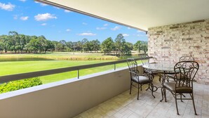 Un balcón con vistas a un campo de golf, un muro de ladrillo y una mesa redonda con sillas.