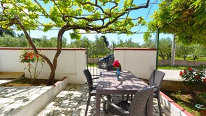 Un patio exterior con una mesa y sillas, rodeado por un jardín con un árbol y flores.