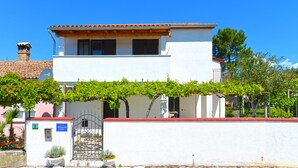Un edificio de dos pisos con fachada blanca, techo de tejas rojas y una pérgola cubierta de hiedra.