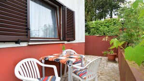An outdoor patio with a table and two chairs, a potted plant, and a window with blinds.