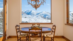 Un'area pranzo con un tavolo rotondo, quattro sedie, un lampadario e un'ampia finestra con vista su una montagna innevata.