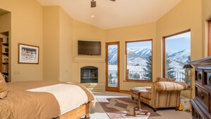 Una camera da letto con un letto, un caminetto, una televisione, un divano e ampie finestre vista montagna.