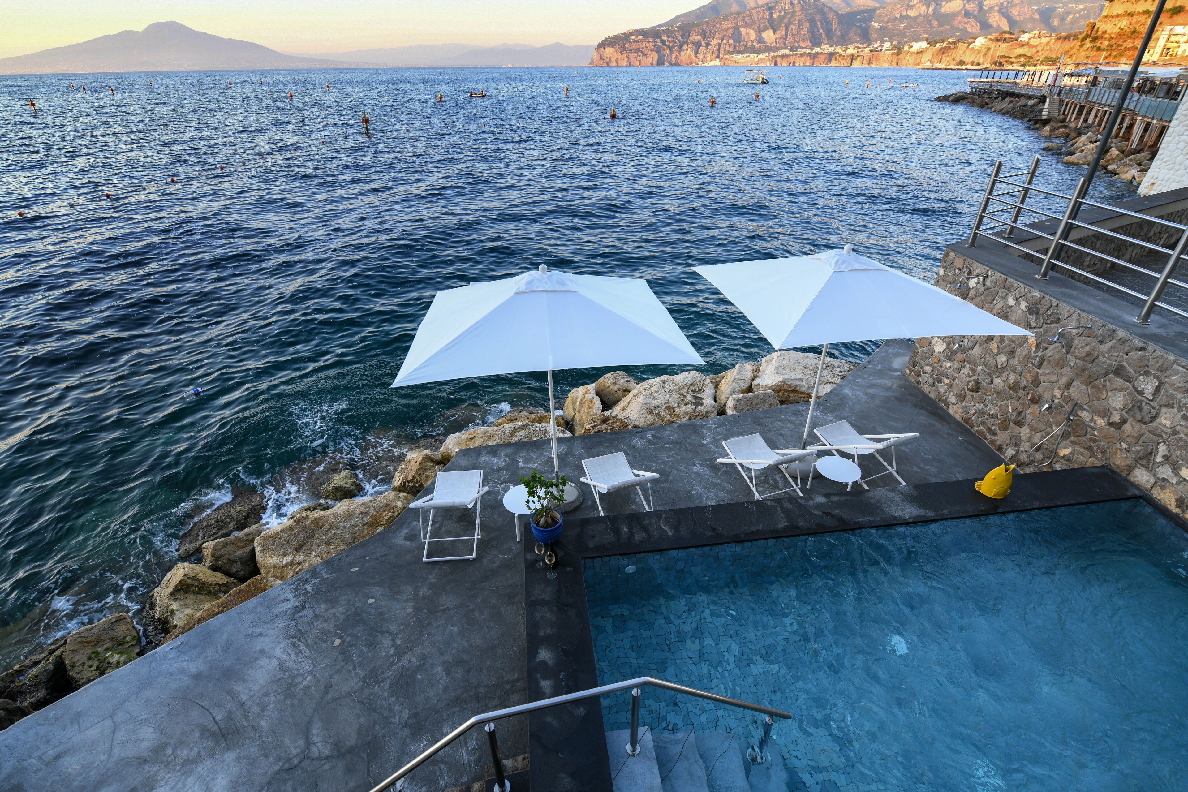 A pool area with white umbrellas, lounge chairs, and a view of the sea.