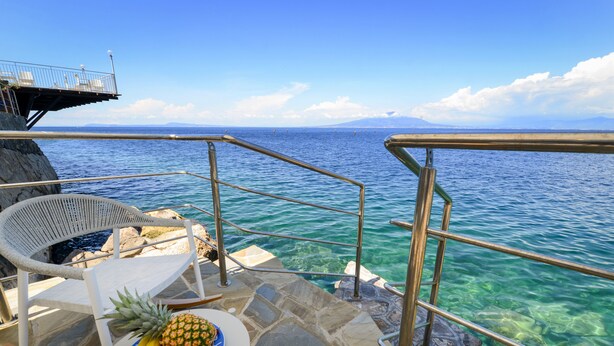 A deck with a table set with fruit, a chair, and a railing overlooking clear blue water. - Beachfront Villa Sorrento & private sea access (Sorrento)