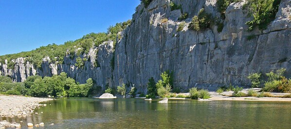 A river with clear water, surrounded by rocky cliffs and sparse vegetation.