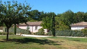 Une villa rose, dotée d’un toit en tuiles, entourée d’une végétation luxuriante et d’arbres.