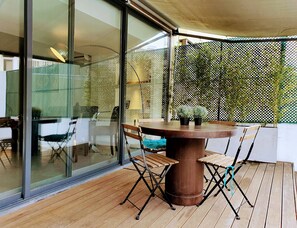 Eine Terrasse mit rundem Tisch und Stühlen, einer Glastür und einem Spalier mit Pflanzen.