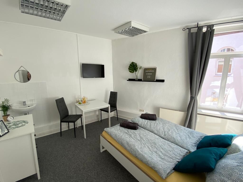 A modern hotel room with a bed, desk, chair, and a TV mounted on the wall.