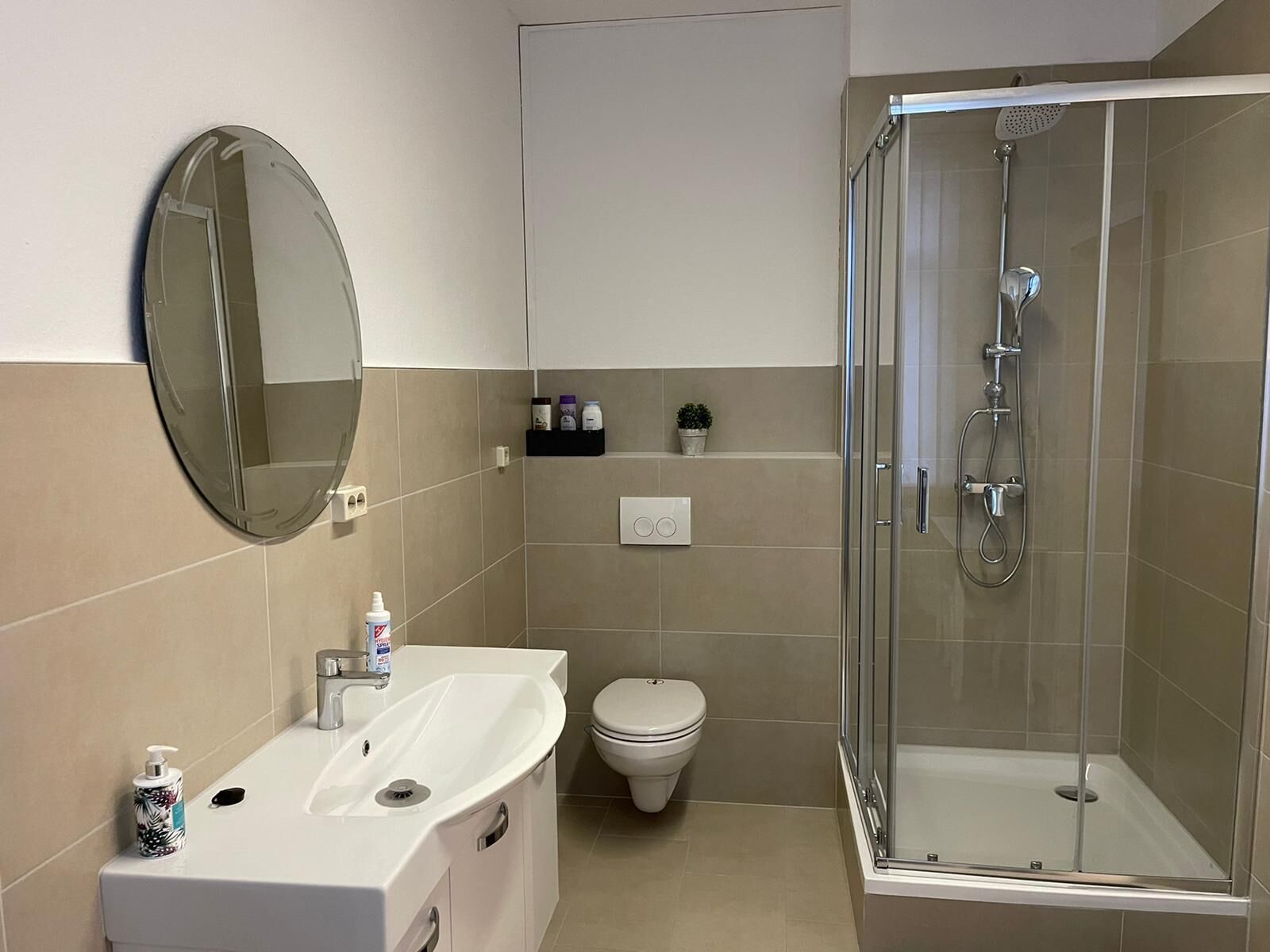 Een badkamer met douche, toilet, wastafel en spiegel.