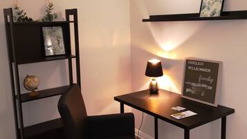 A small office space with a desk, chair, bookshelf, and a wall-mounted shelf with a framed welcome sign.
