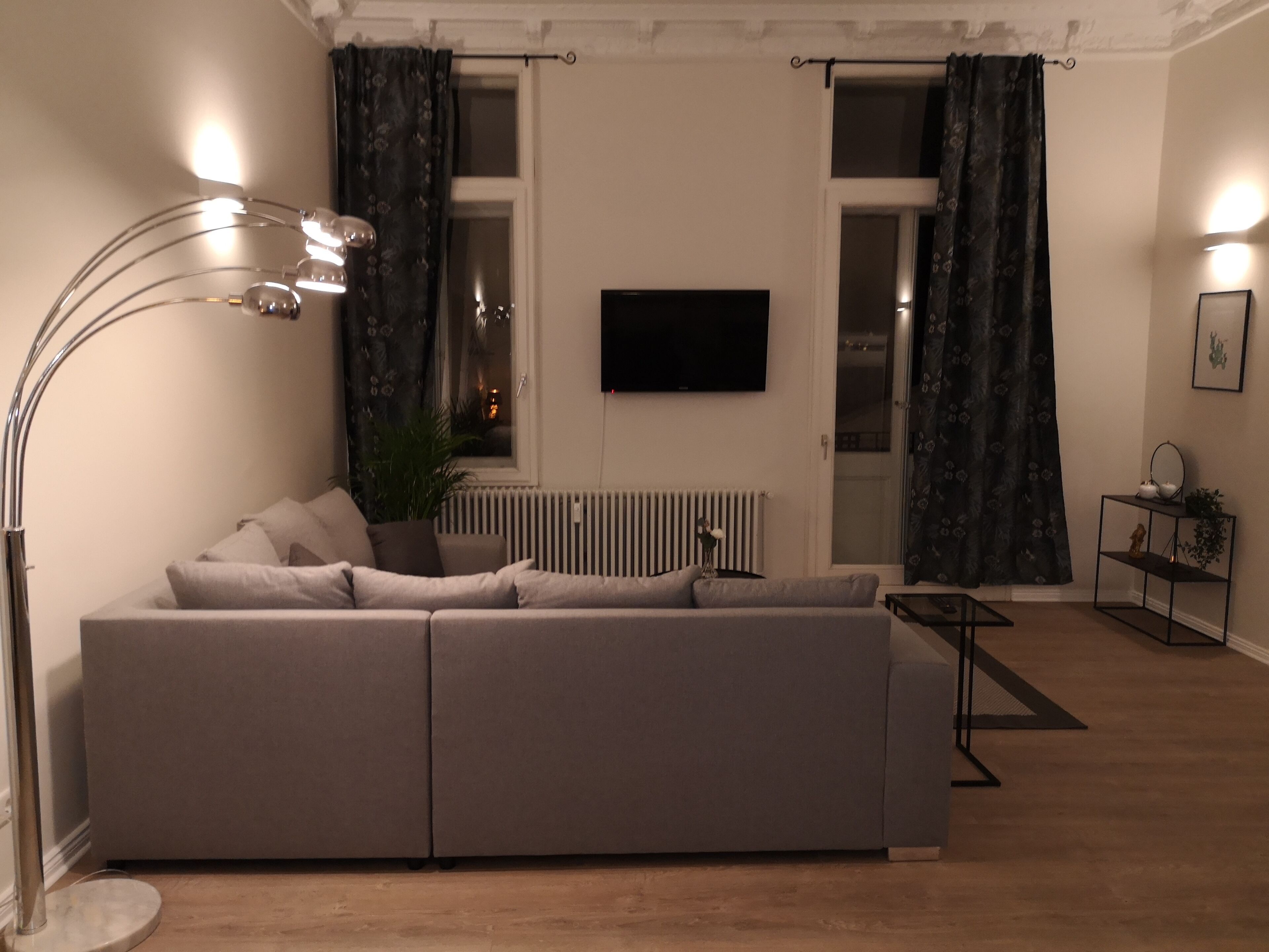 Una sala de estar moderna con un sofá modular, una lámpara de pie, un televisor montado en la pared y un radiador.
