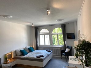 A modern bedroom with a bed, a desk, a chair, a window, and a plant.