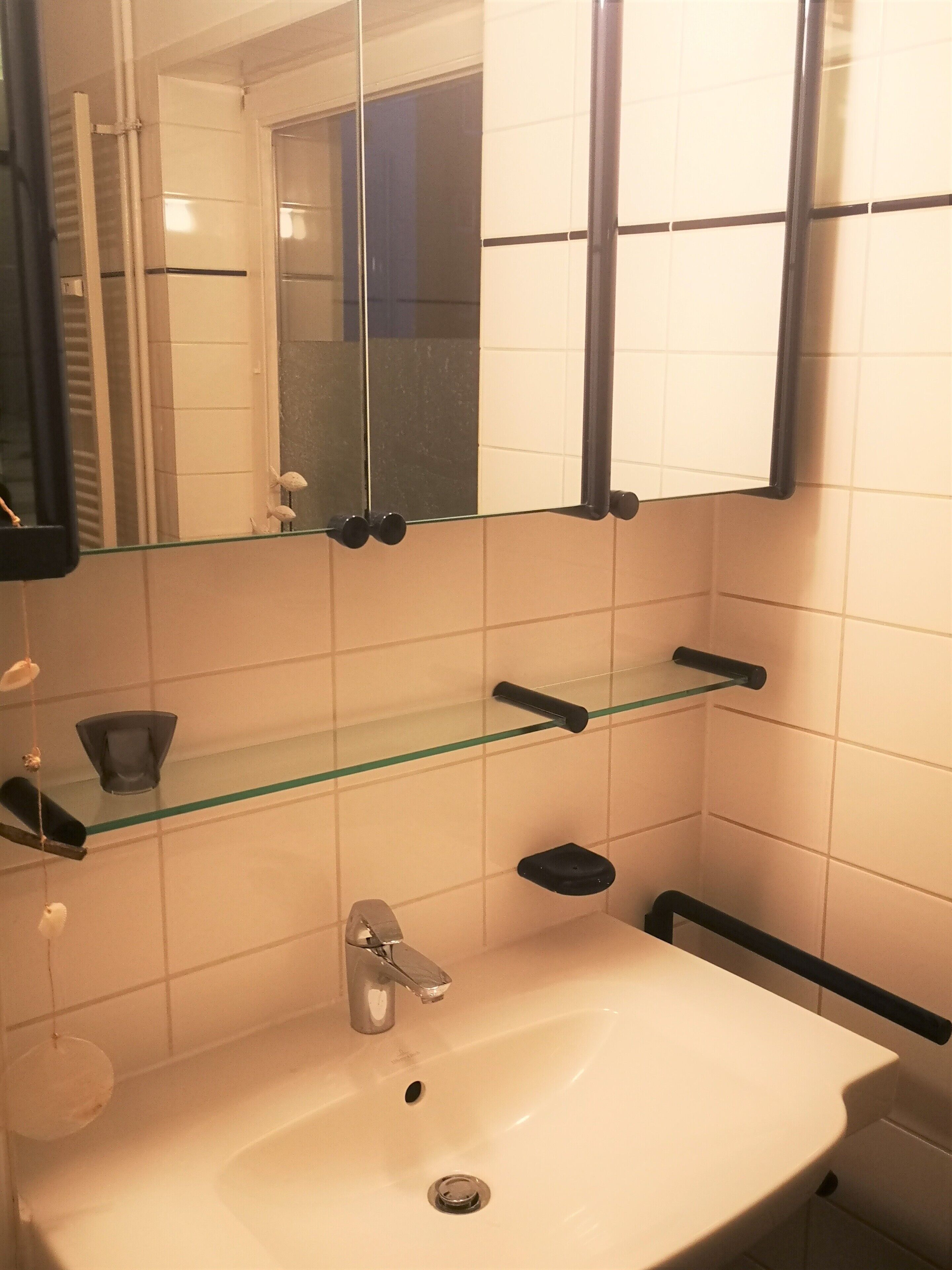 Een badkamer met een witte wastafel, een spiegel en een glazen plankje.