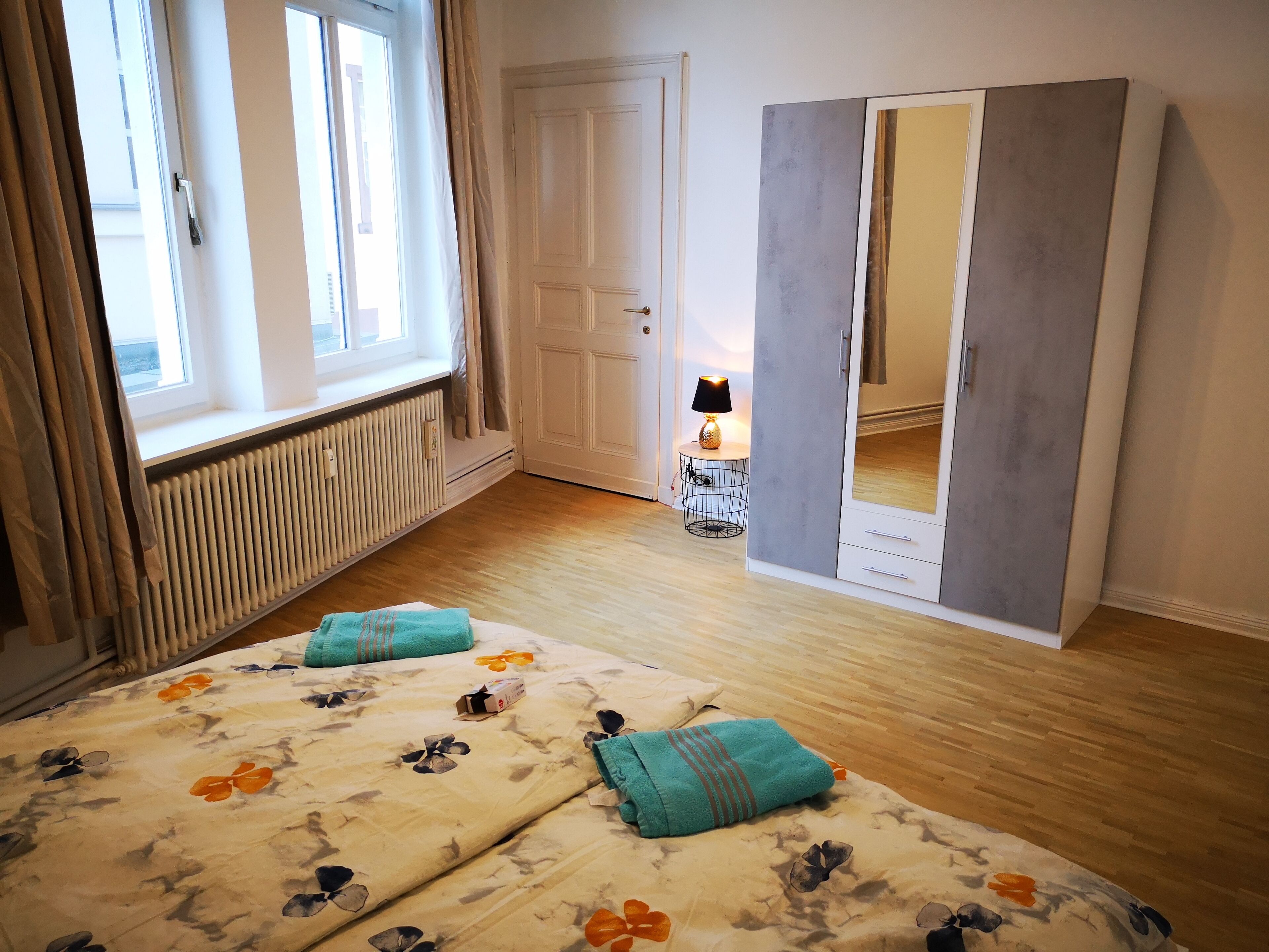 Et soveværelse med seng, skab, radiator, et vindue og en lampe.