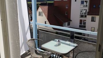 Un balcon avec une table et des chaises, donnant sur un quartier résidentiel avec des maisons et un paysage vallonné.