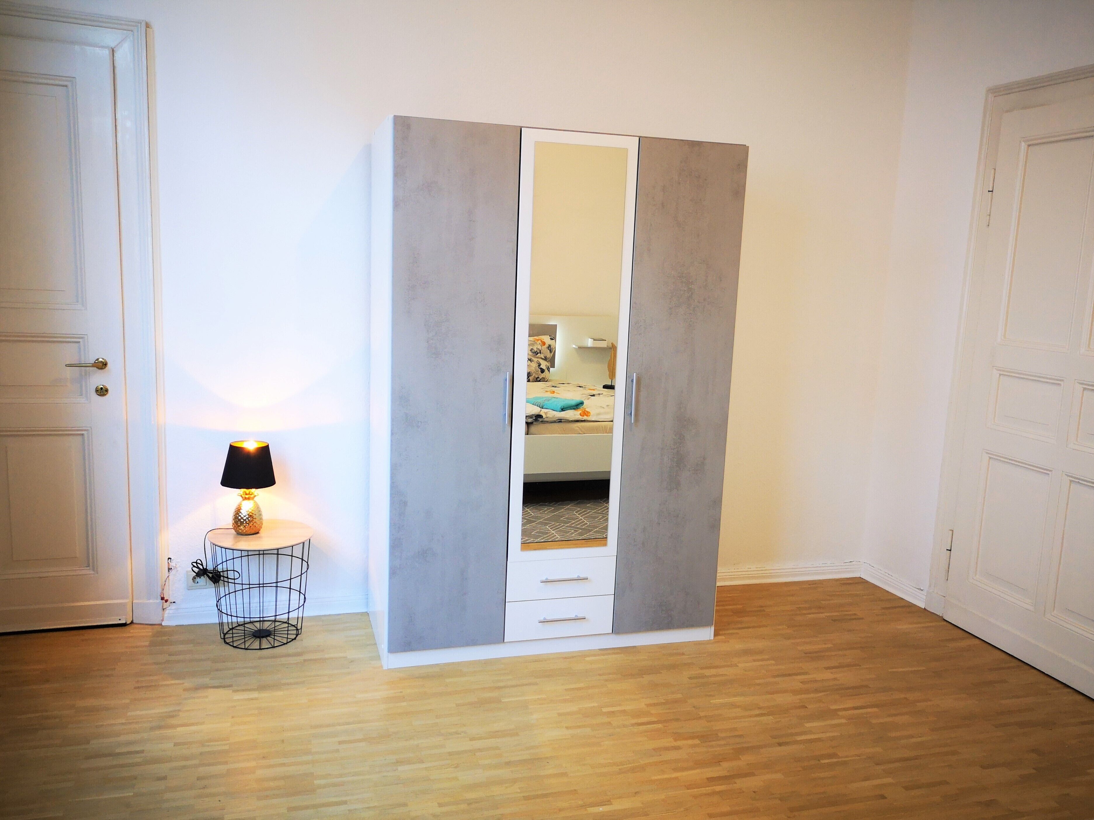 Una habitación con armario, lámpara y cama al fondo.