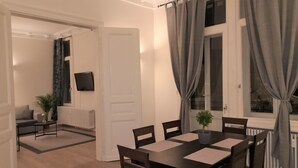 Un comedor con una mesa y sillas, un televisor en la pared y vistas al exterior a través de una ventana con cortinas.