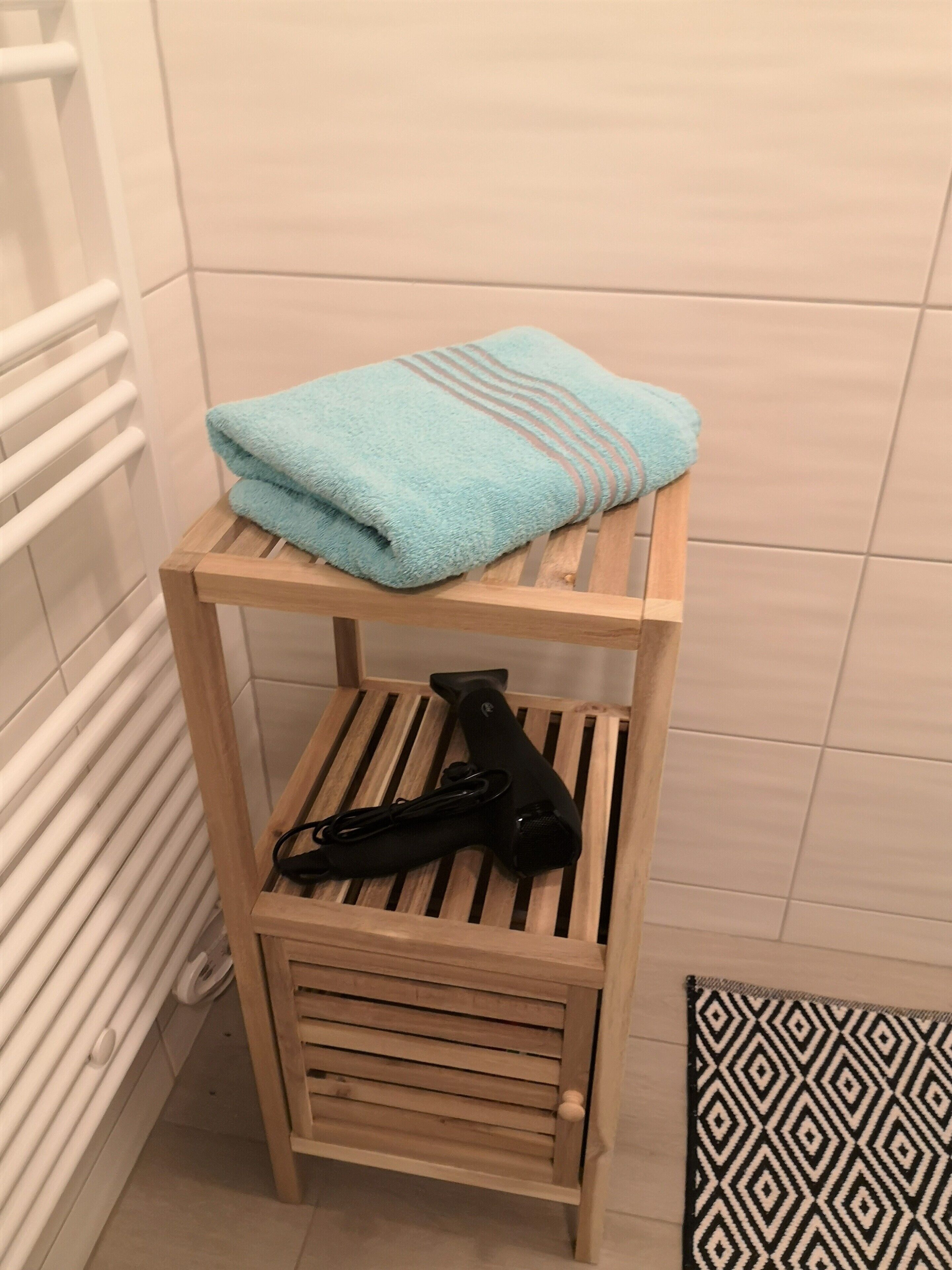 A small wooden shelf with a folded blue towel and a black hairdryer.