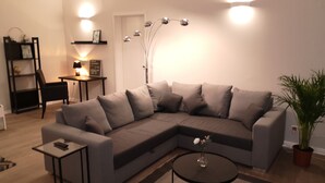 Una sala moderna con un sofá modular, una pequeña mesa redonda de centro y una lámpara de pie.