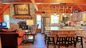 Un interno rustico con un camino in pietra, mobili in legno, una cucina con un piano di lavoro in granito e un'ampia finestra.