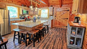Cucina in stile baita con elementi in legno, un'isola centrale, sgabelli da bar, frigorifero, forno a microonde e macchina per il caffè.