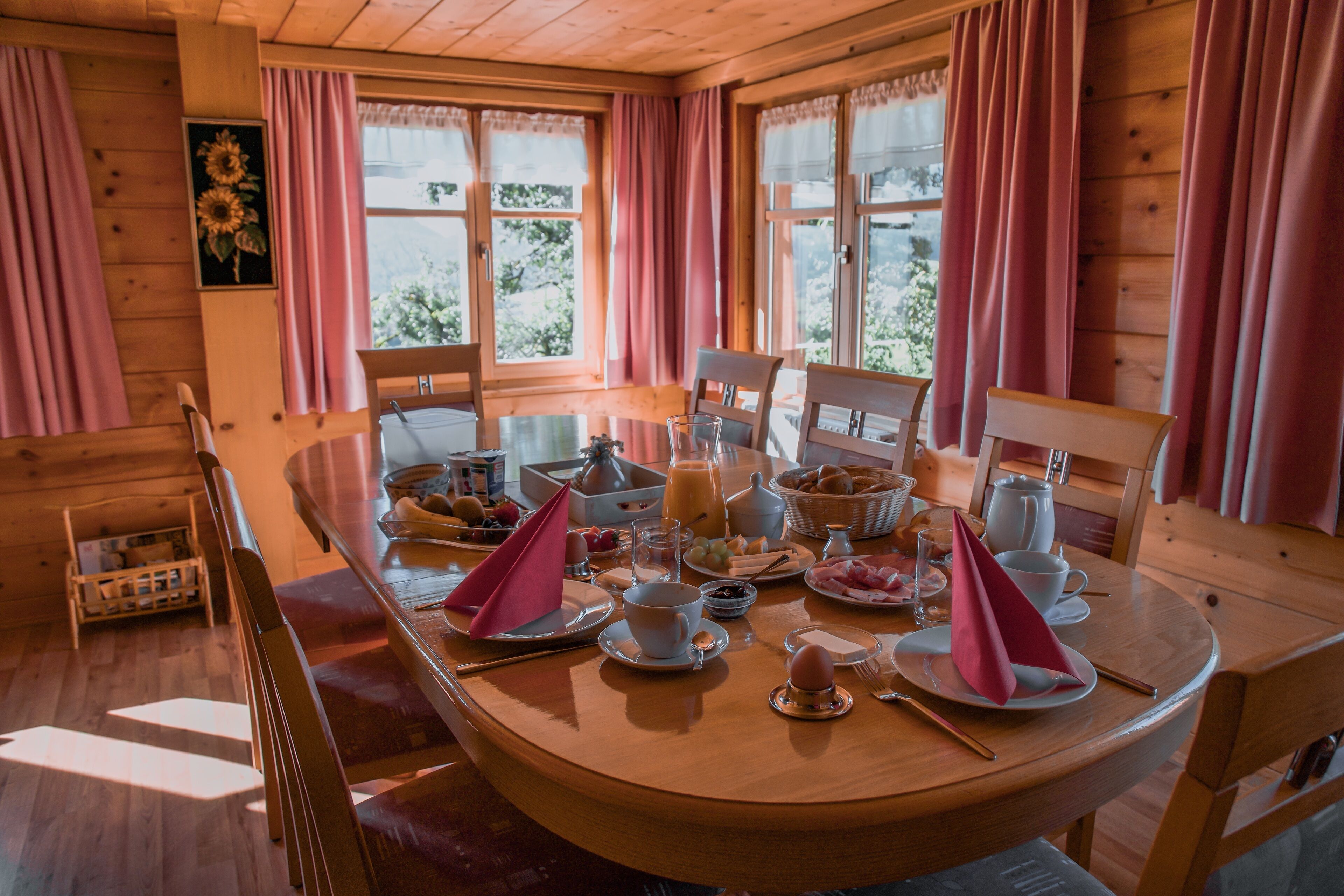 A wooden dining table set for breakfast with various dishes, cups, and a pitcher.