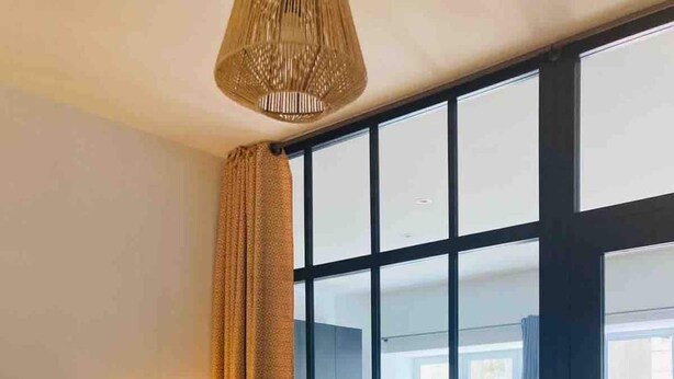 Habitación de hotel con cama, mesita de noche, lámpara, ventana con cortinas y vista al interior.