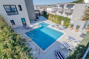 A rooftop pool with lounge chairs, a pergola, and a view of the city.