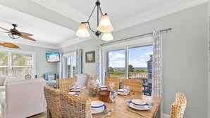 A dining area with wicker chairs, a wooden table set for four, and a ceiling fan. - One Wave or Another: Gulf Views, Private Pool, Putting Green (Indian Pass)
