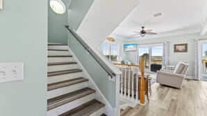 A staircase with wooden steps and white railings leading to a living area with a ceiling fan, a television, and a view of the outdoors. - One Wave or Another: Gulf Views, Private Pool, Putting Green (Indian Pass)