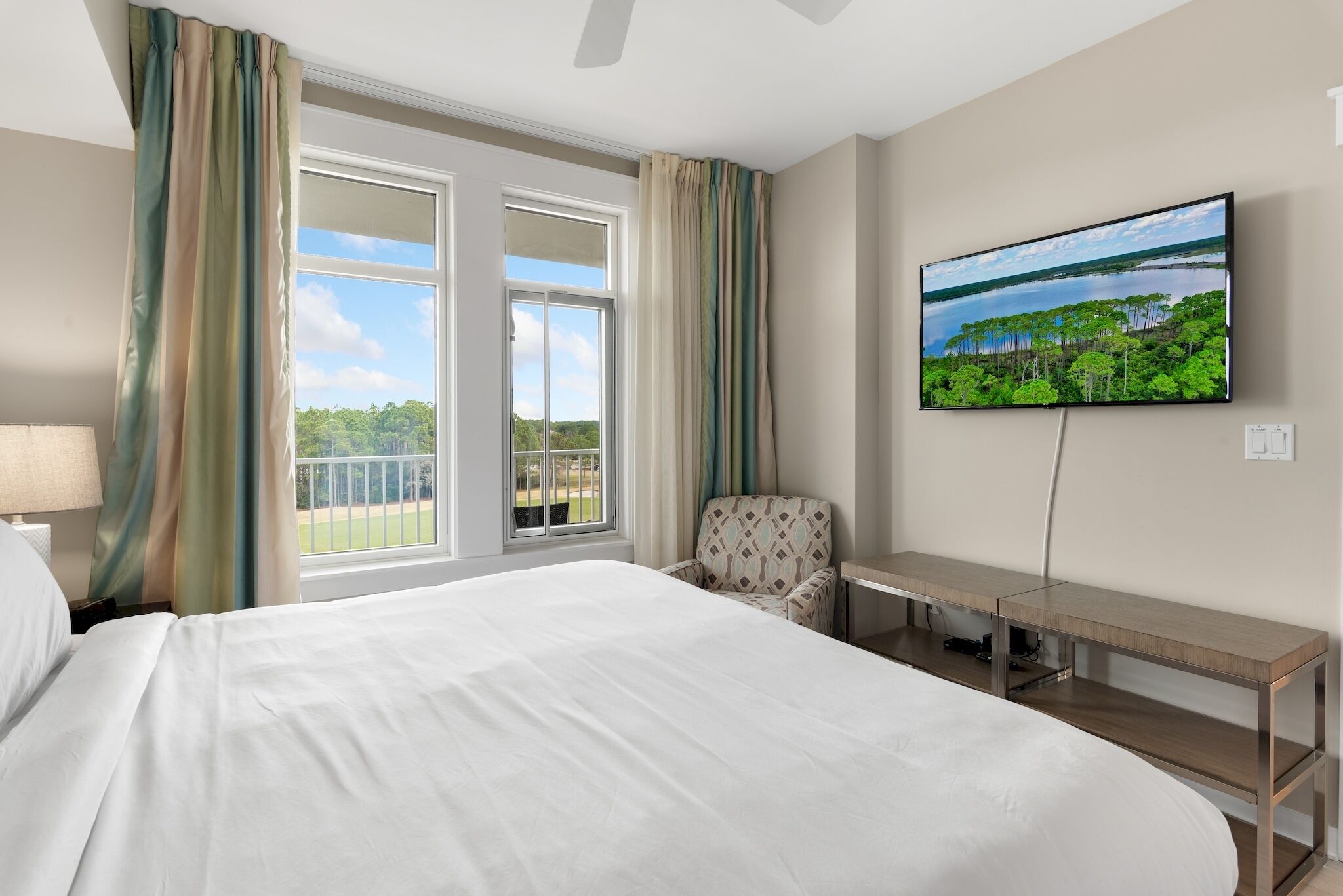 Habitación de hotel con una cama grande, un escritorio, una silla, un televisor en la pared y vistas al exterior a través de la ventana.