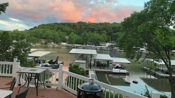 Vista sul lago con barche ormeggiate, un gazebo e una terrazza con sedie e tavoli.