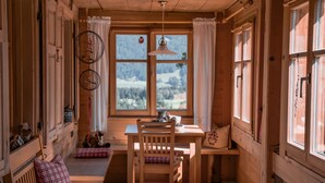 A cozy wooden cabin with a wooden table and chairs, a bench, and a window with a view of a snowy landscape.